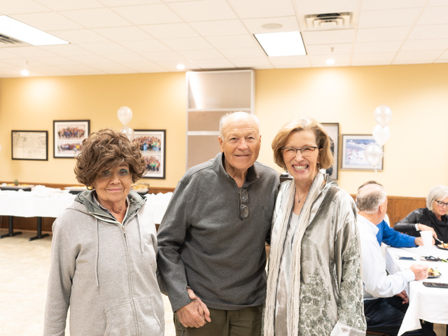 CEO Shirley Barnes talks with former county commissioner Dan Erhart and his wife Kathy Erhart.  Description: Two women are on either side of one man. All three are facing the camera smiling.